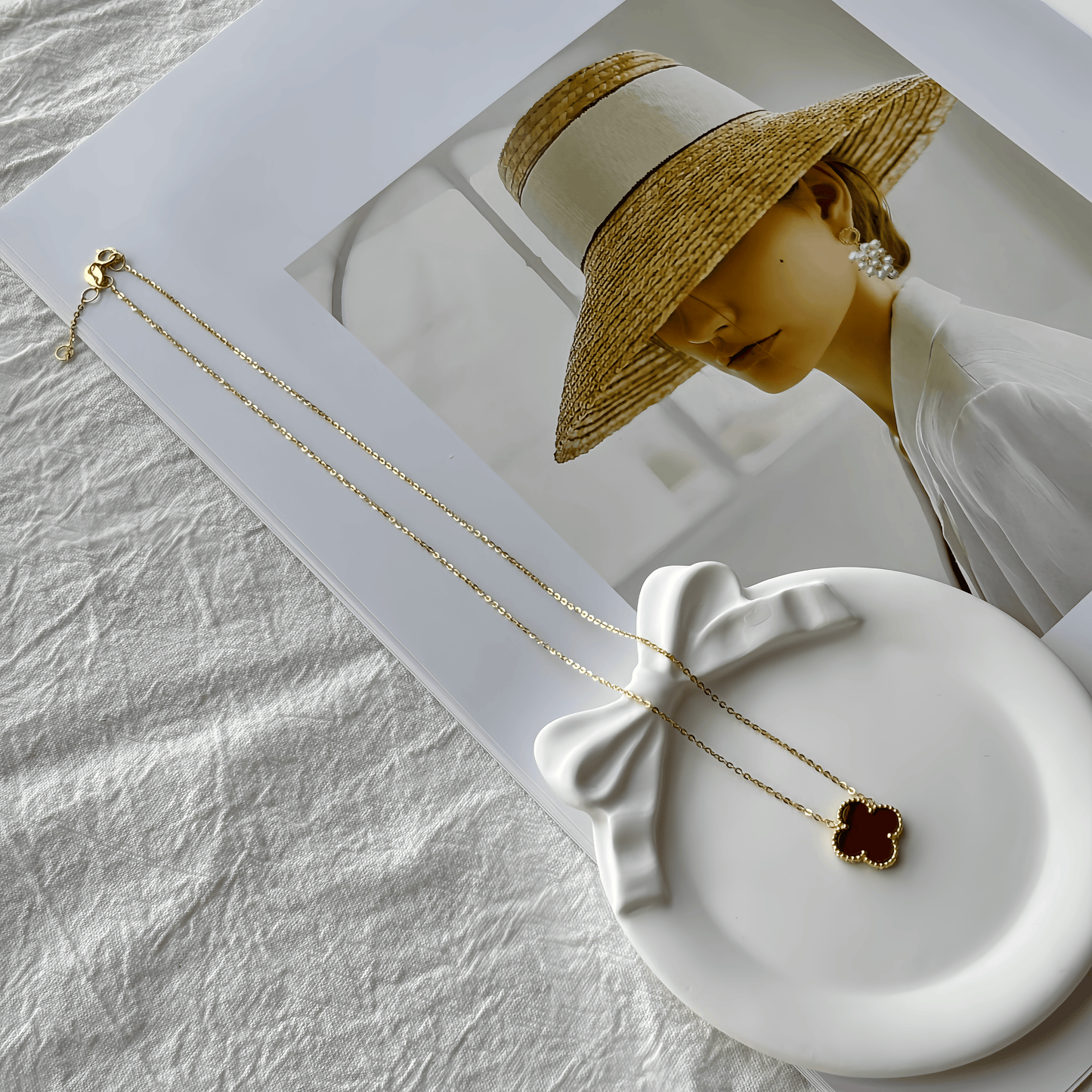 Gold necklace with a clover pendant on a white dish, with a person wearing a hat in the background.