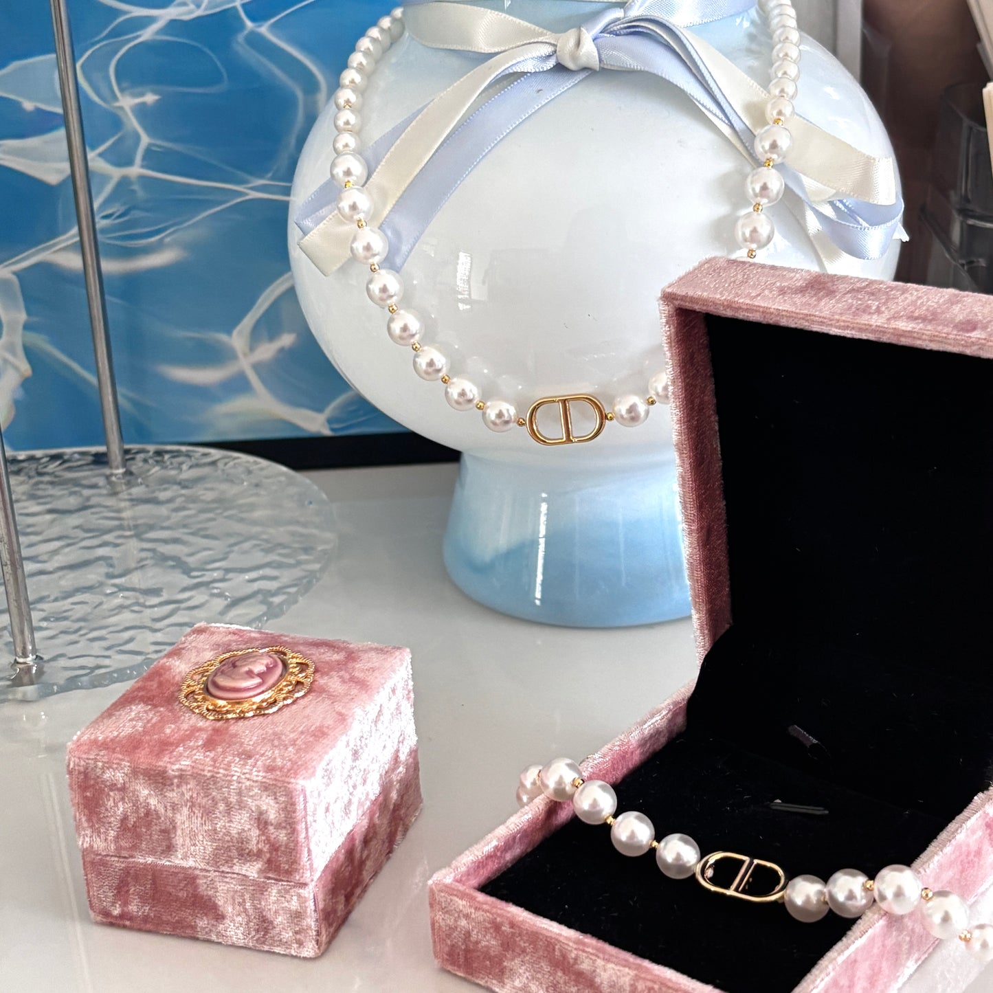 Pearl necklace with gold clasp on a pink velvet stand and box against a blue marble background