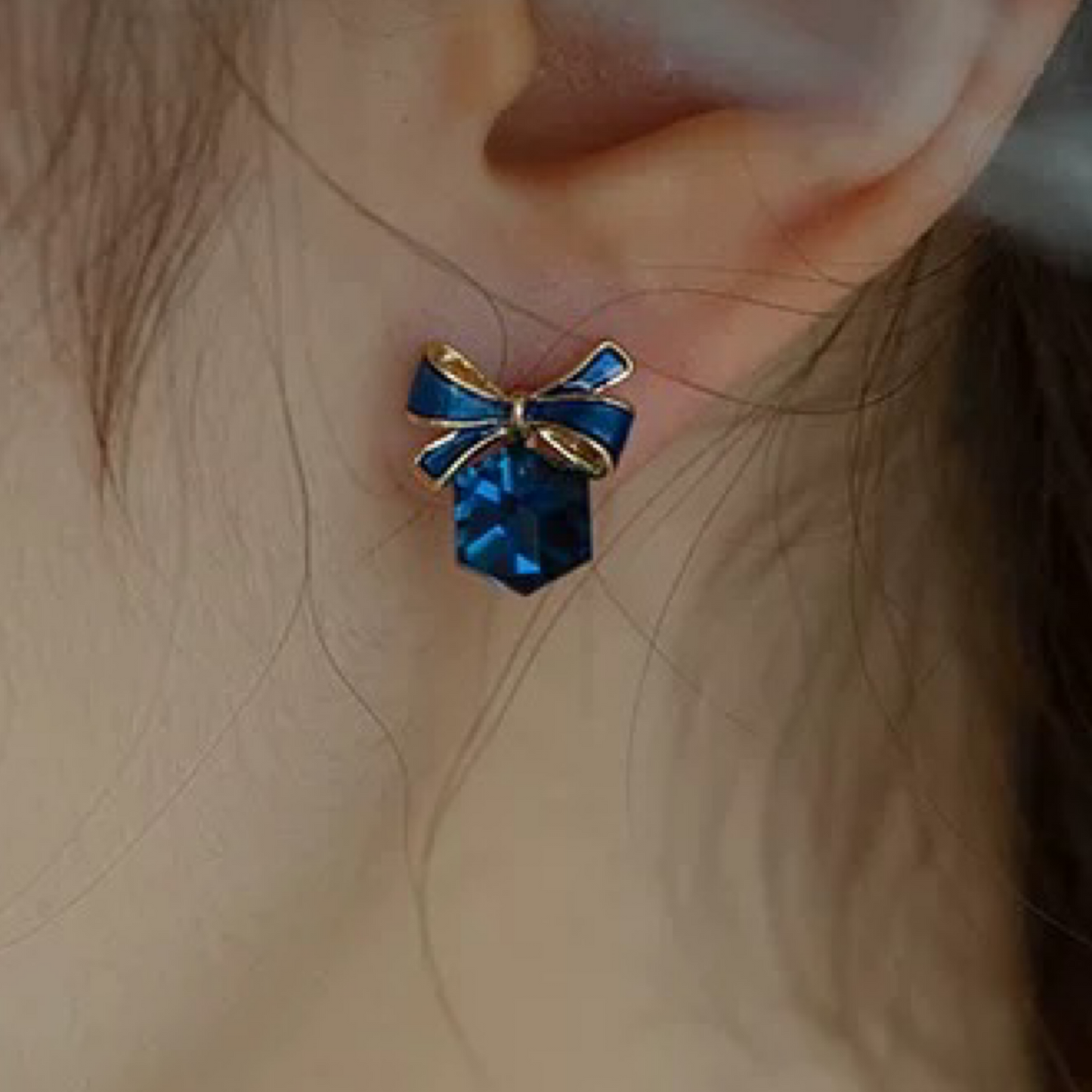 Blue bow-shaped earring worn on an ear