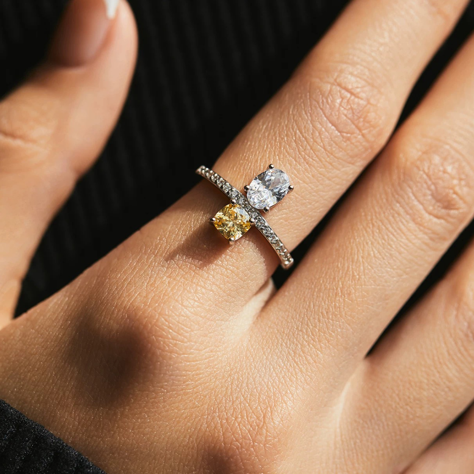 Close-up of a hand wearing a silver ring with yellow and clear gemstones.