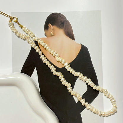 Woman wearing a long pearl necklace with a minimal background