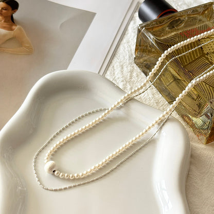 Pearl necklace on a white dish with a bottle of perfume in the background