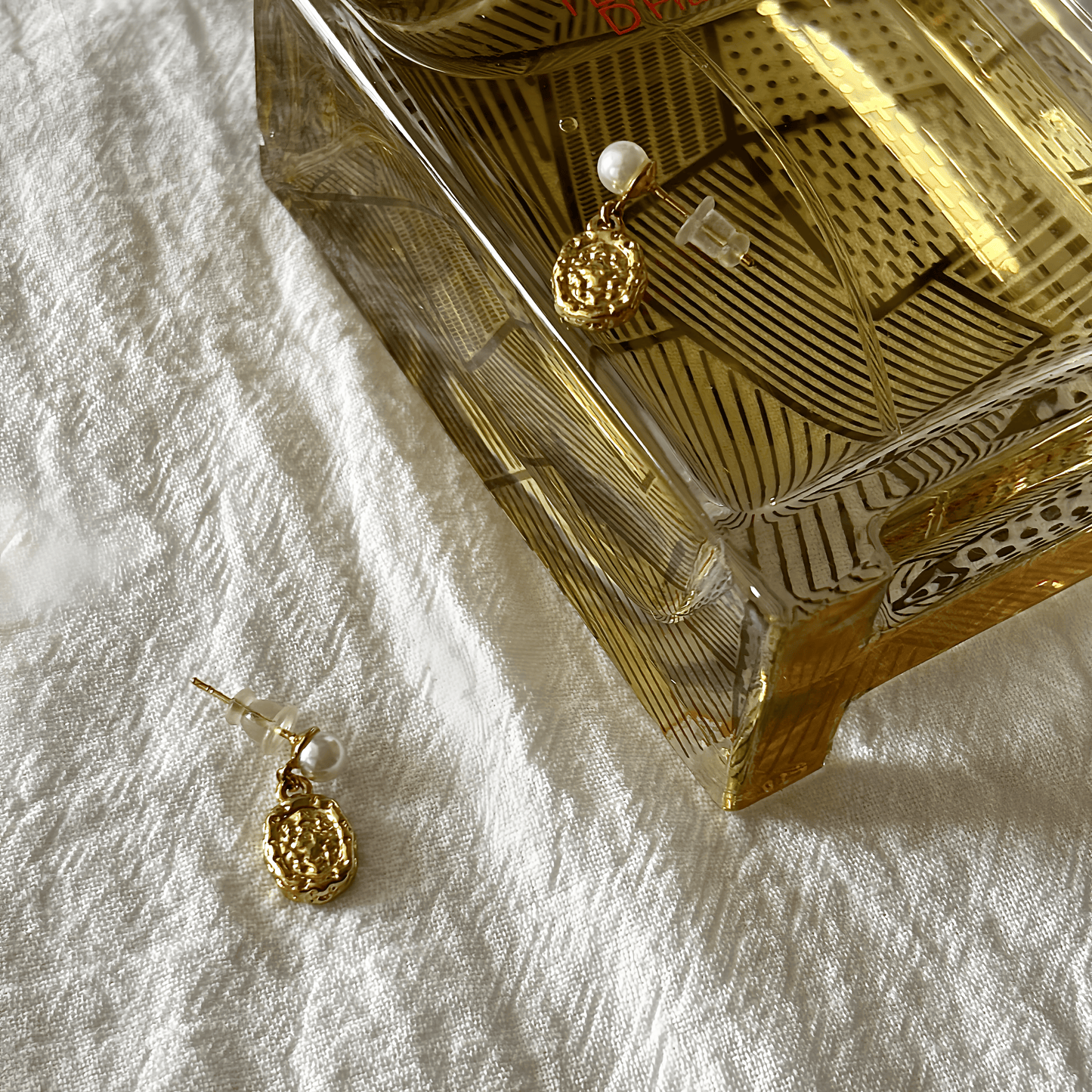 Gold earrings on a textured white surface with a decorative box in the background.