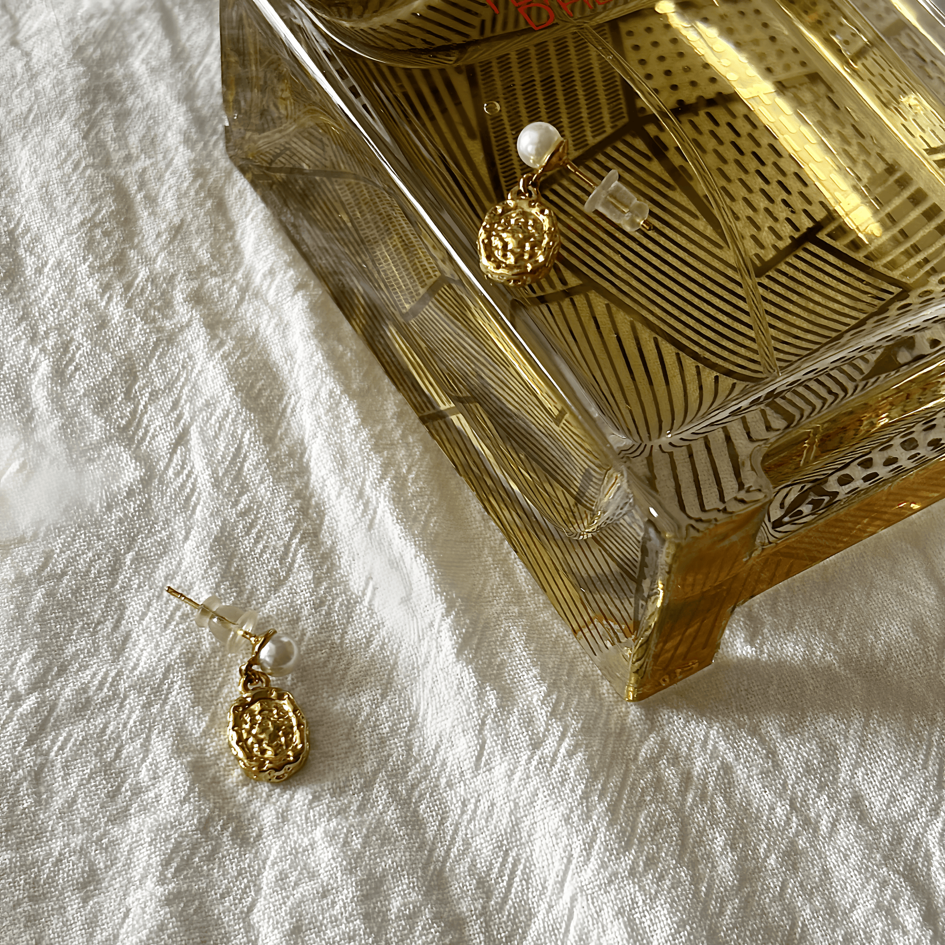 Gold earrings on a textured white surface with a decorative box in the background.