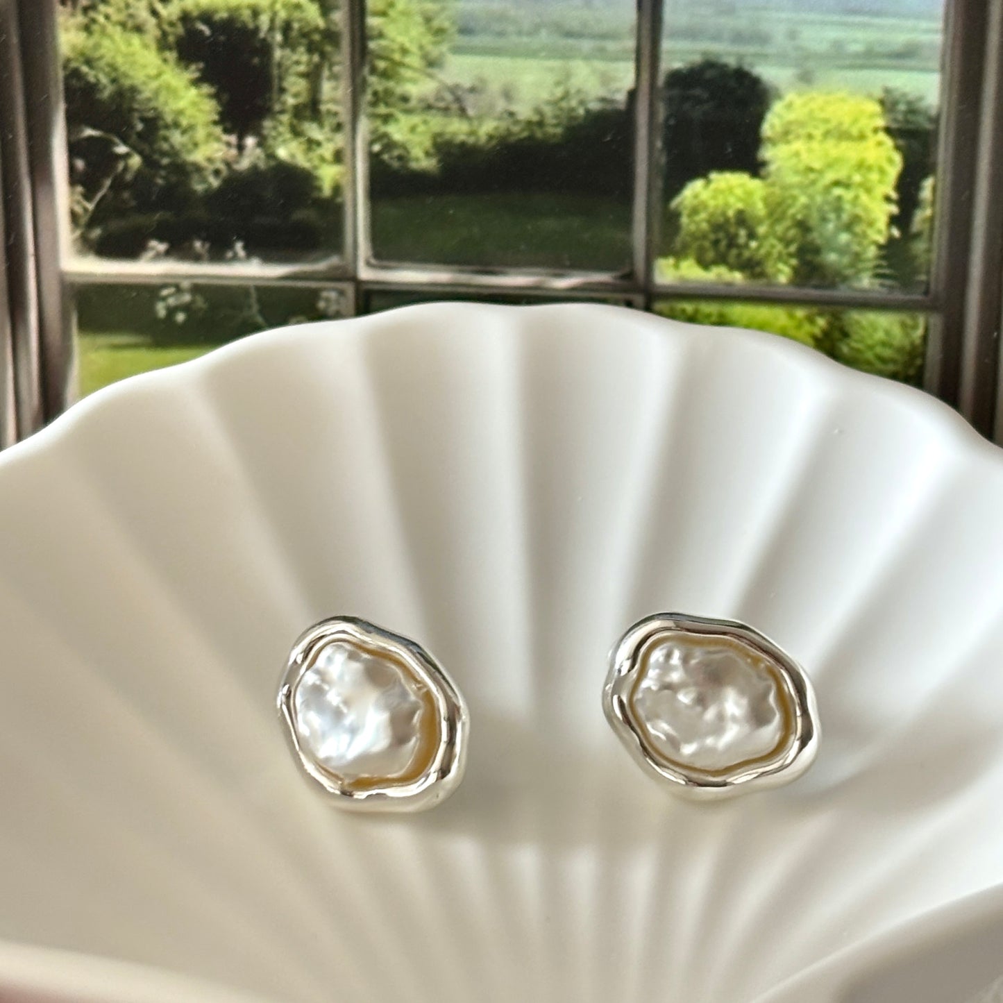 Pair of silver earrings with pearl-like centers on a shell against a window view.