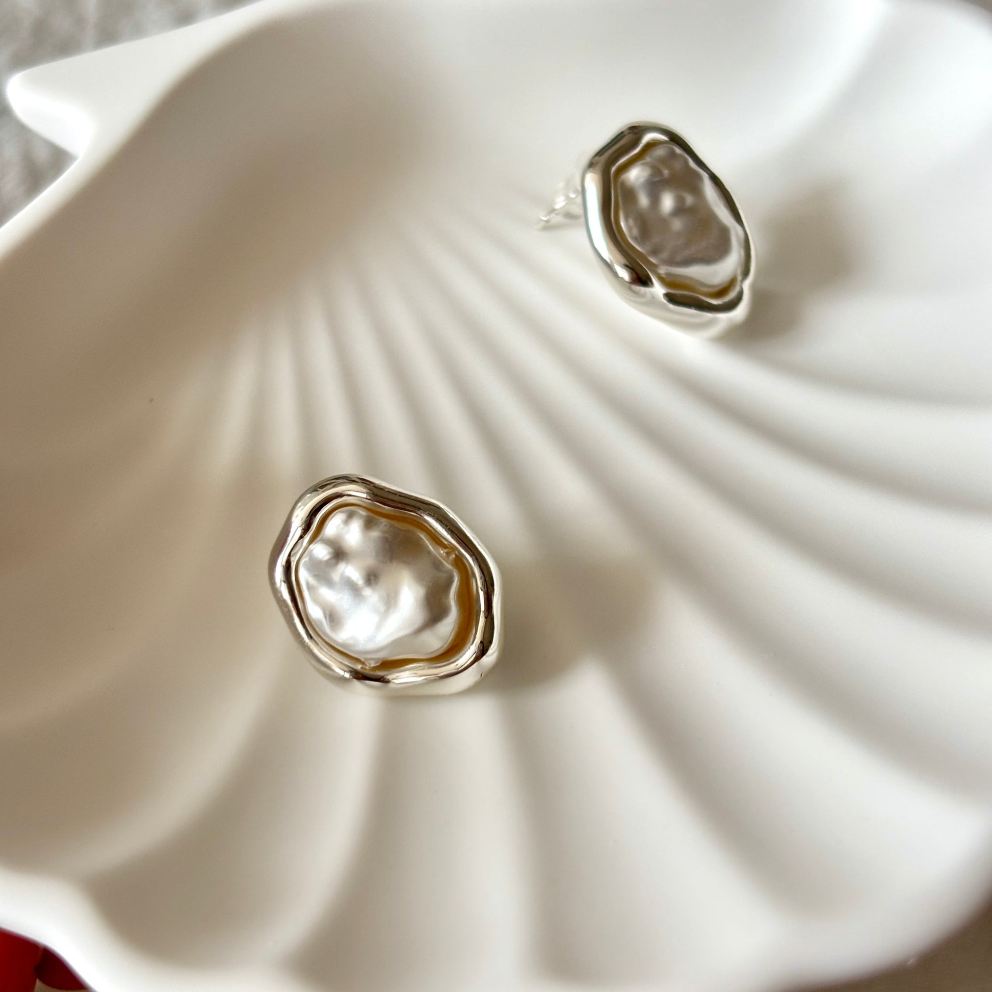 Silver earrings with a natural pearl design on a white shell background