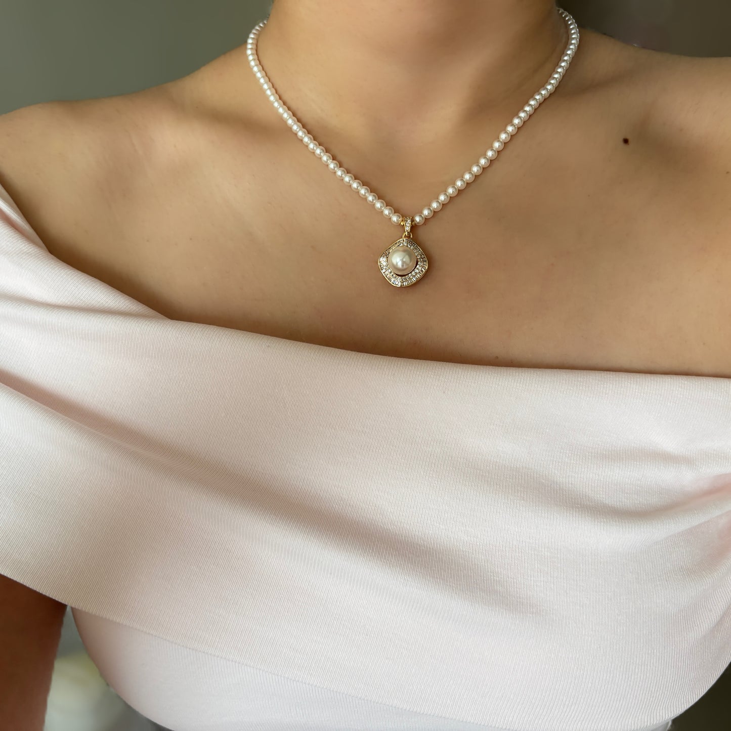 Pearl necklace with a pendant on a person wearing a light pink top.