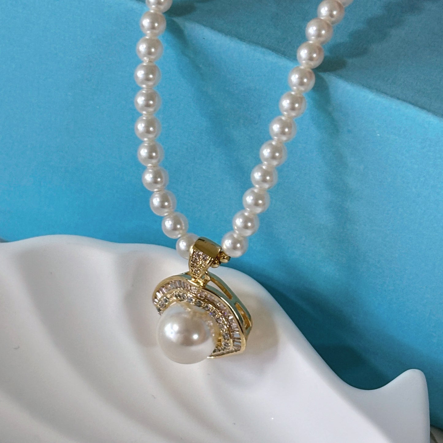 Pearl necklace with a gold and pearl pendant on a white surface with a blue background