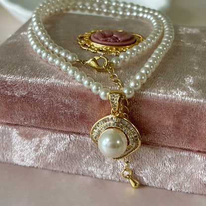 Pearl necklace with gold pendant on a textured pink surface