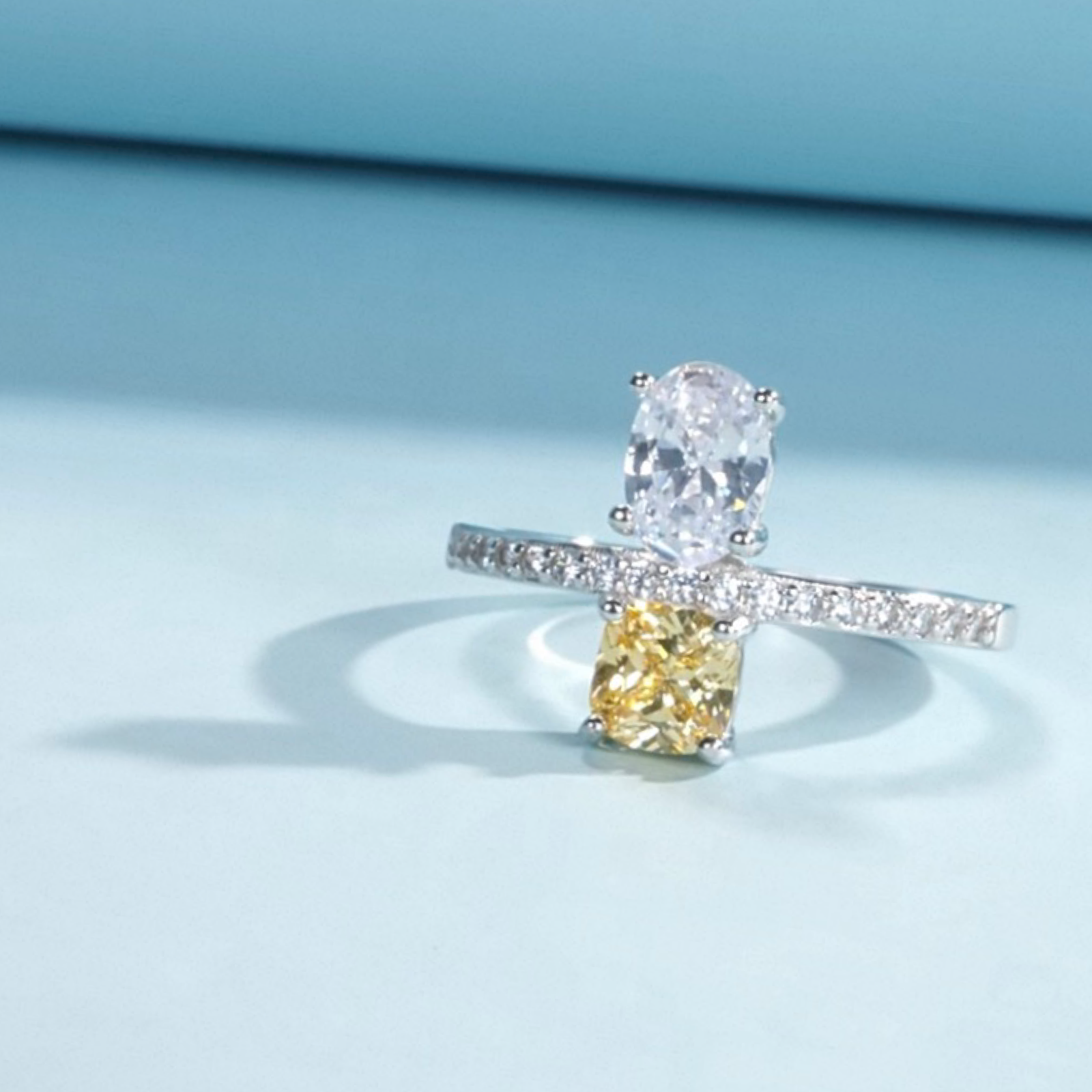 Diamond ring with a pear-shaped yellow diamond and round white diamonds on a light blue background