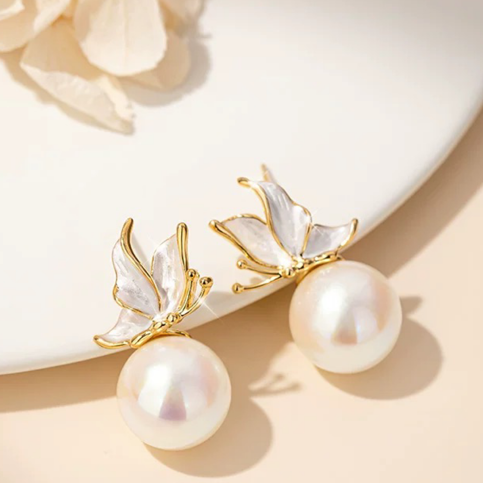 Pearl earrings with gold leaf detailing on a beige surface