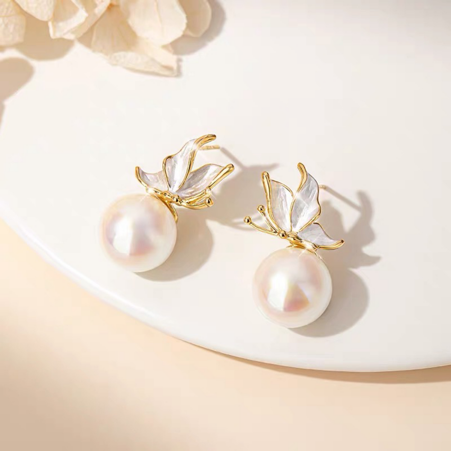 Pearl earrings with gold leaf accents on a soft beige background