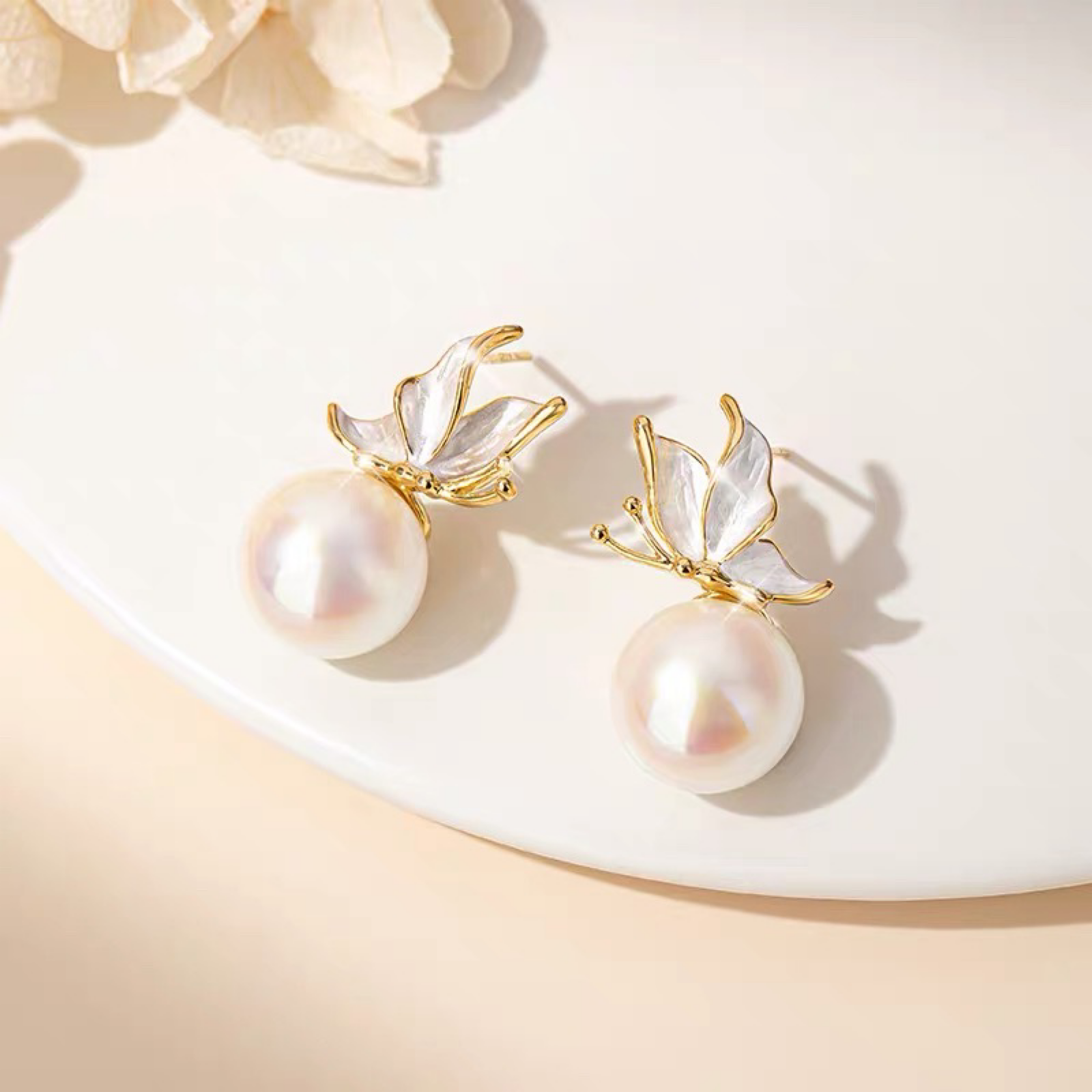 Pearl earrings with gold leaf accents on a soft beige background