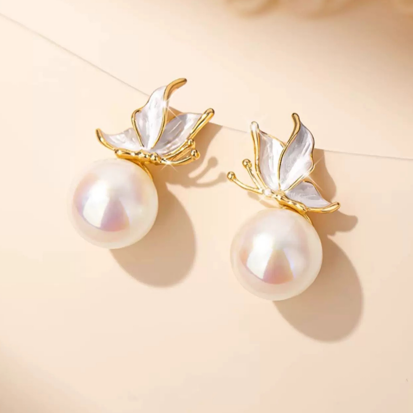 Pearl earrings with gold leaf-like attachments on a beige background