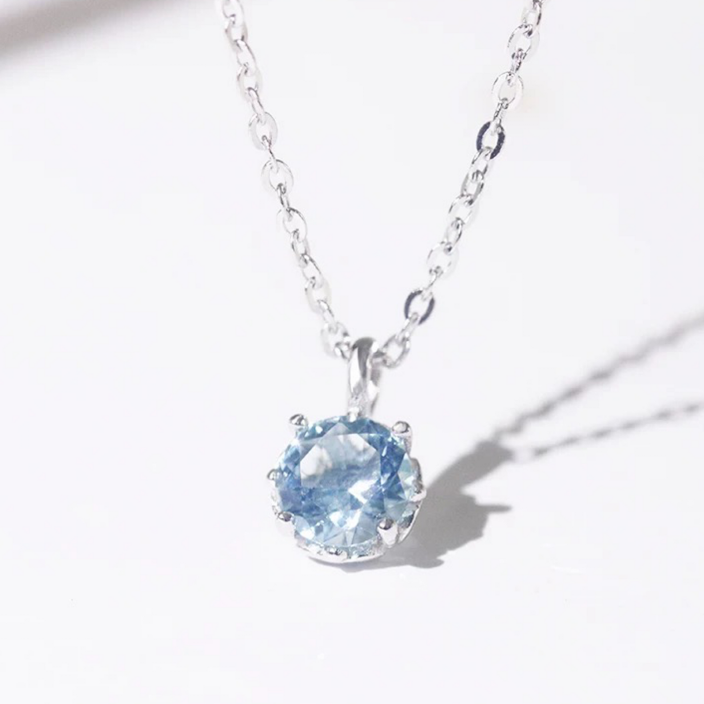 Silver necklace with a blue gemstone pendant on a white background with shadow