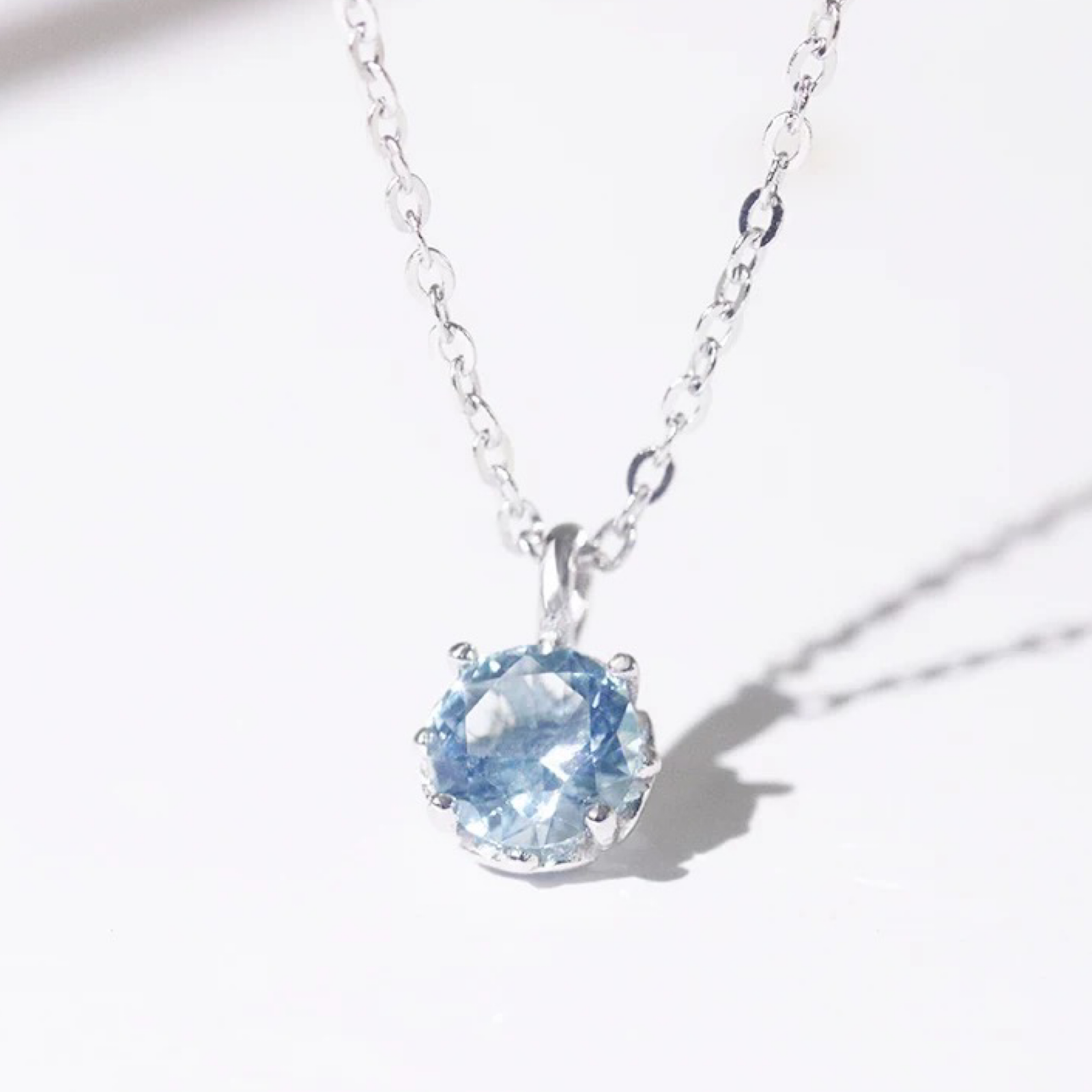 Silver necklace with a blue gemstone pendant on a white background with shadow