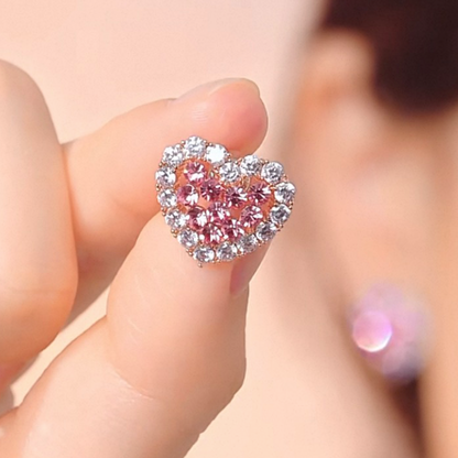 Heart-shaped pink gemstone earring held between fingers against a blurred background