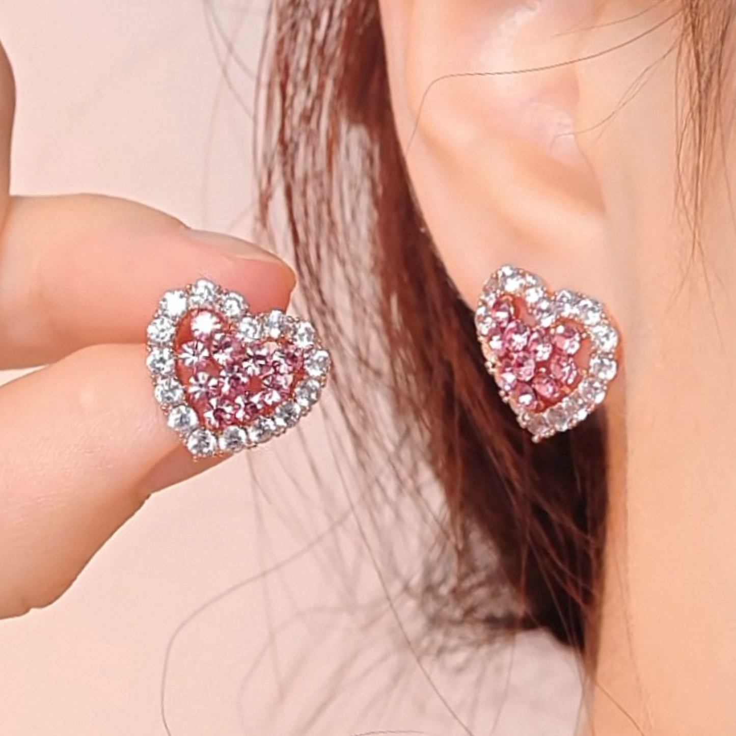 Heart-shaped earrings with pink and silver design worn by a person.