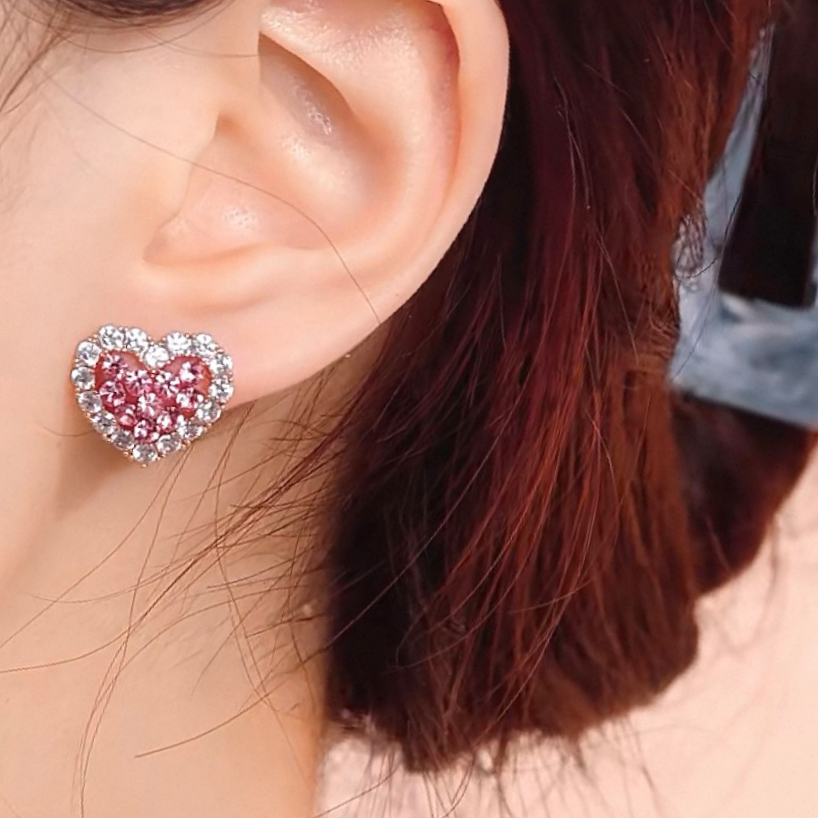 Close-up of a heart-shaped earring worn by a person with brown hair.