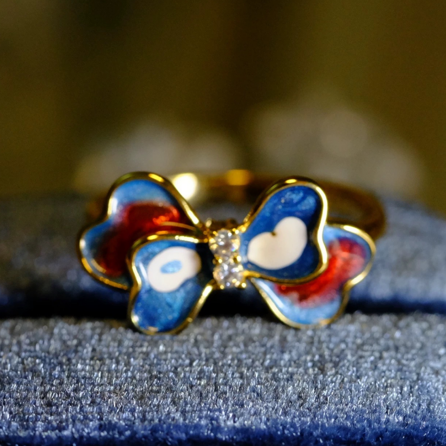 Gold ring with blue and red bow design on a textured surface