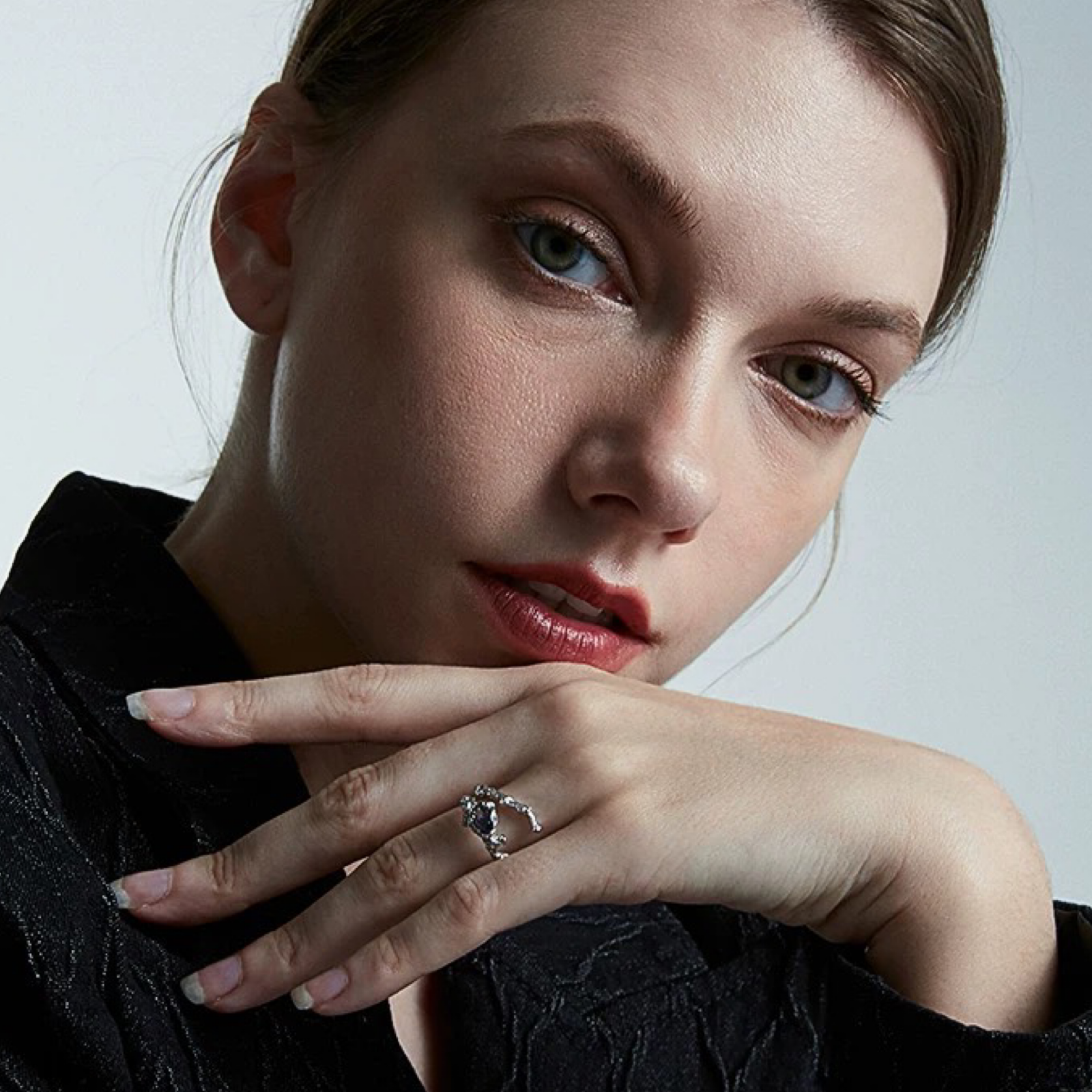 Close-up of a woman wearing a ring with a diamond on a neutral background