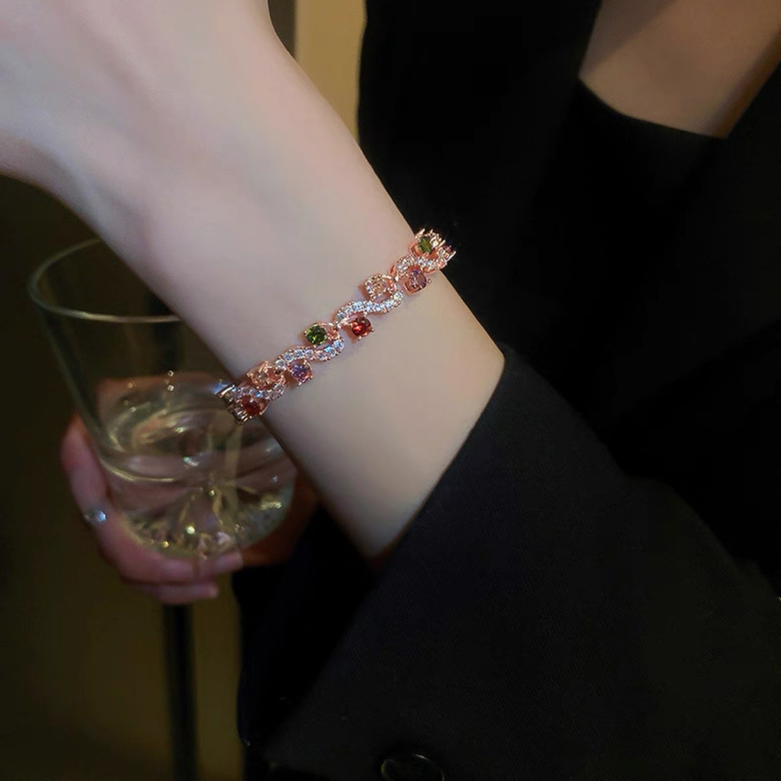 Person wearing a decorative bracelet holding a glass of white wine.