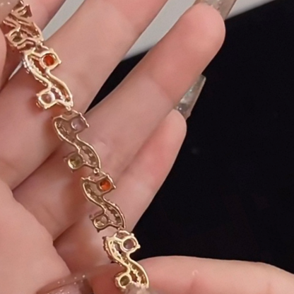 Gold bracelet with red stones held between fingers against a dark background