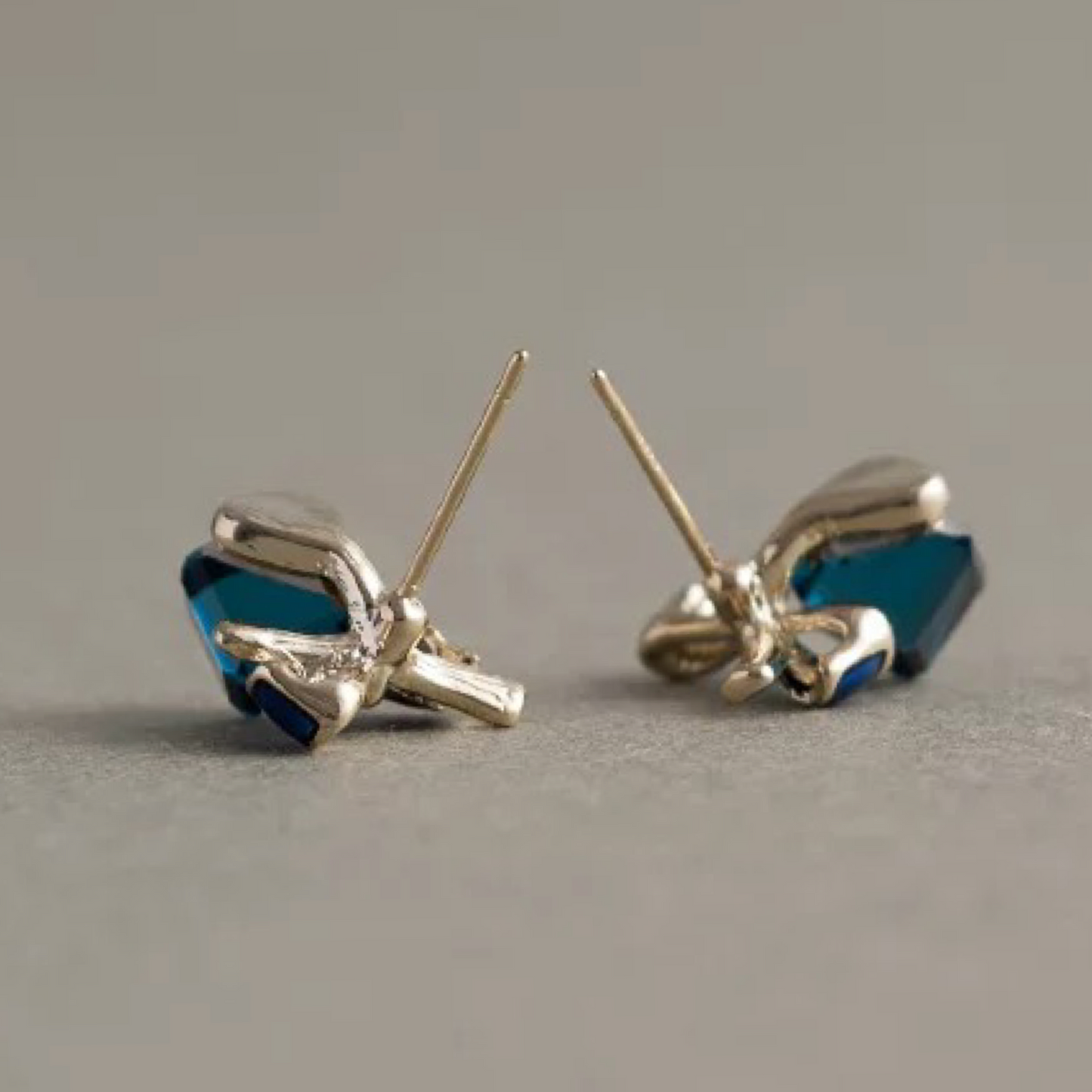 Pair of gold bow-shaped earrings with blue stones on a gray background