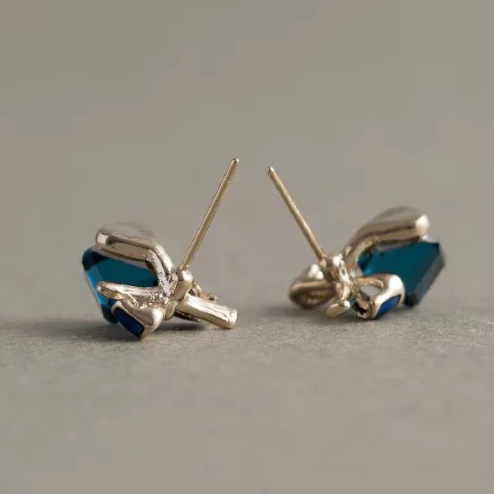 Pair of gold bow-shaped earrings with blue stones on a gray background