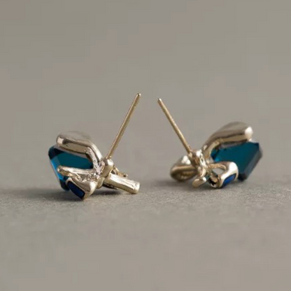 Pair of gold bow-shaped earrings with blue stones on a gray background