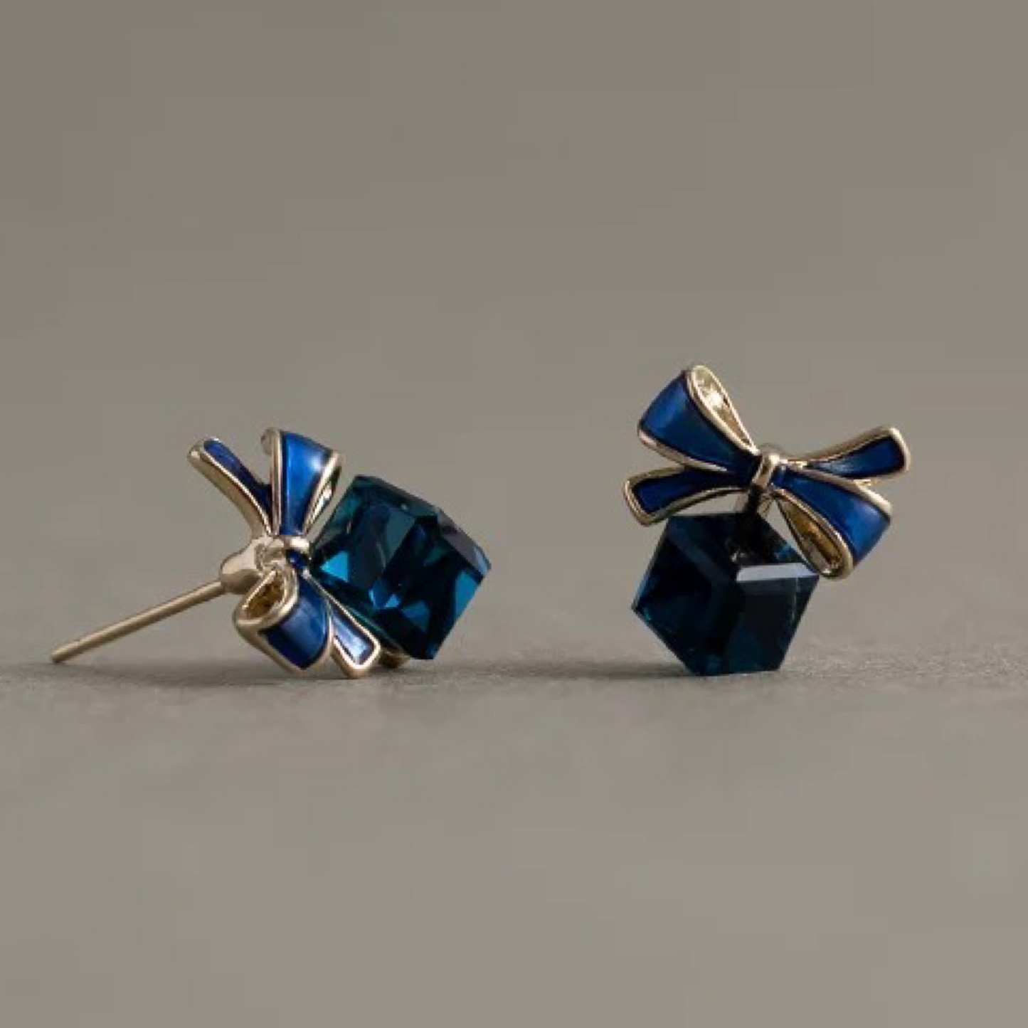 Pair of blue gemstone earrings with gold bows on a gray background