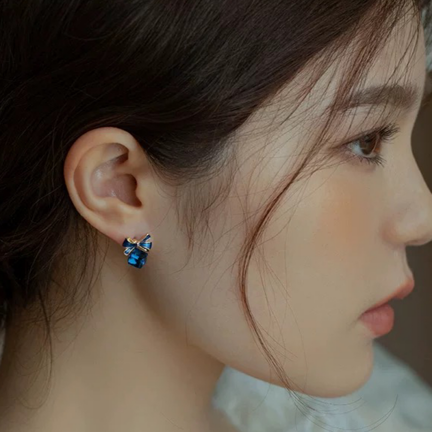 Close-up of a person wearing blue earrings with a blurred background