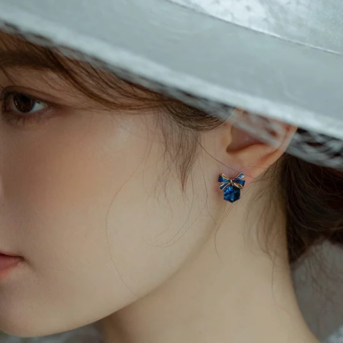 Close-up of an ear wearing a blue gemstone earring with a neutral background