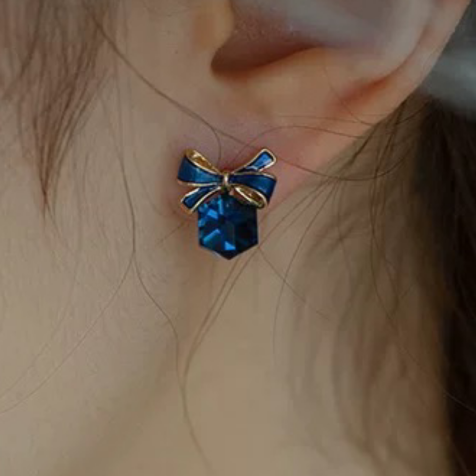 Blue bow-shaped earring worn on an ear