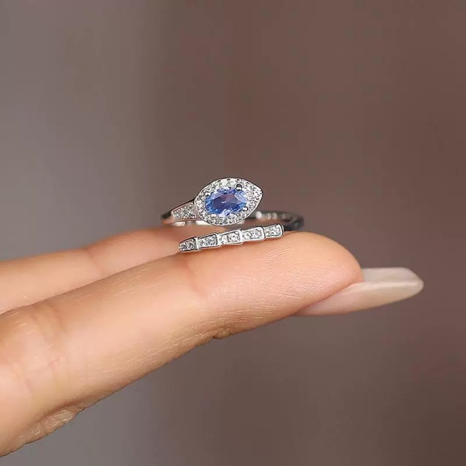 Ring with a blue gemstone on a finger against a neutral background