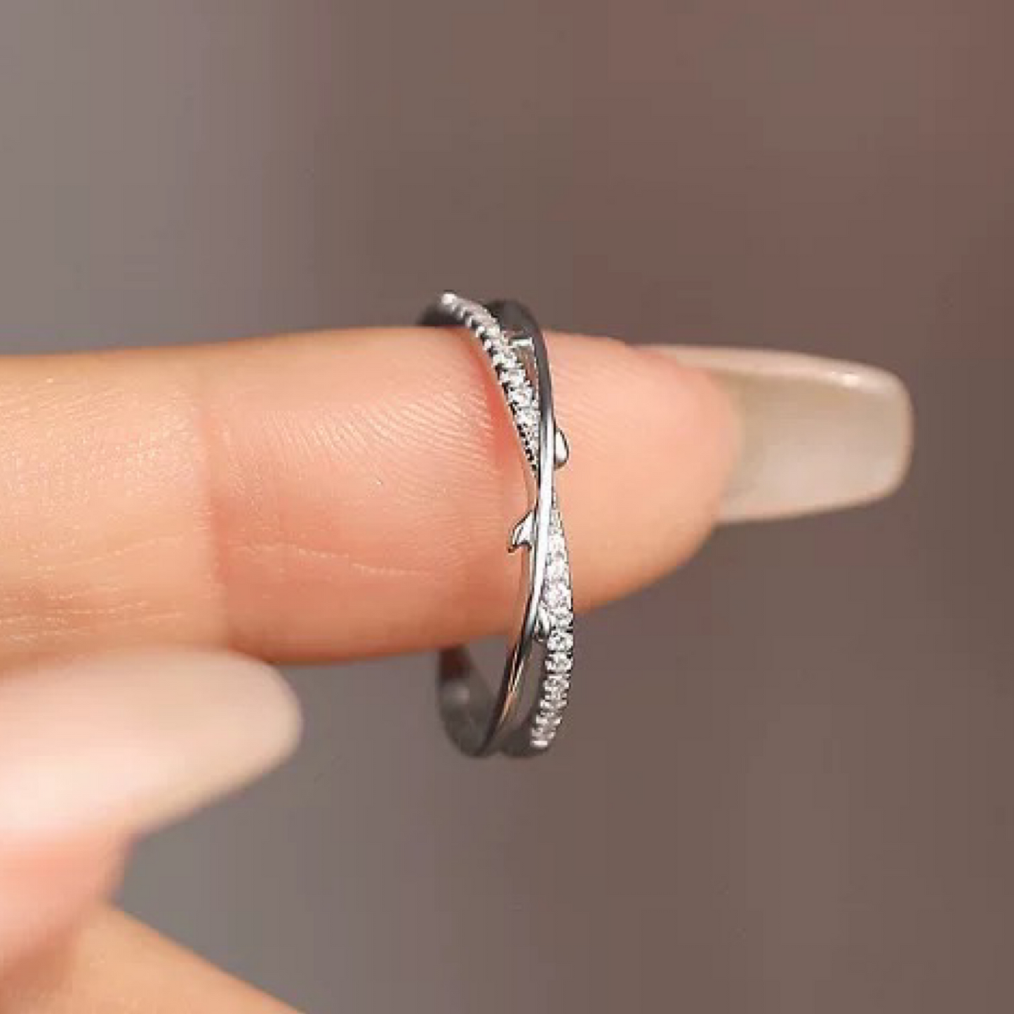 Silver ring with diamond accents on a finger against a neutral background